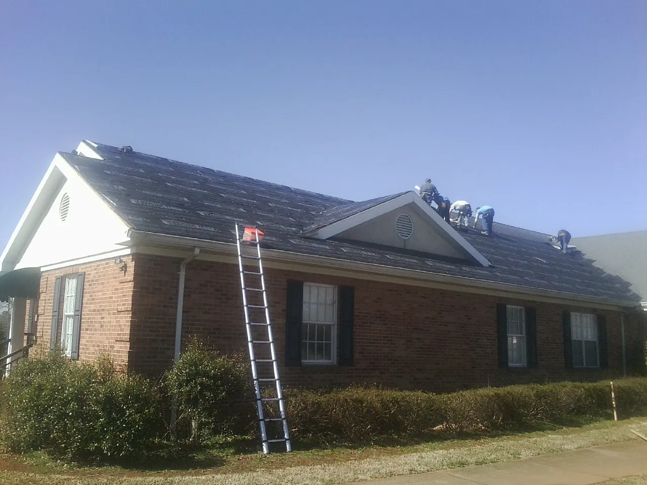 Crew tearing shingles off a brick ranch roof with a ladder set — Emergency Roof Repair work by our crew in Codorus