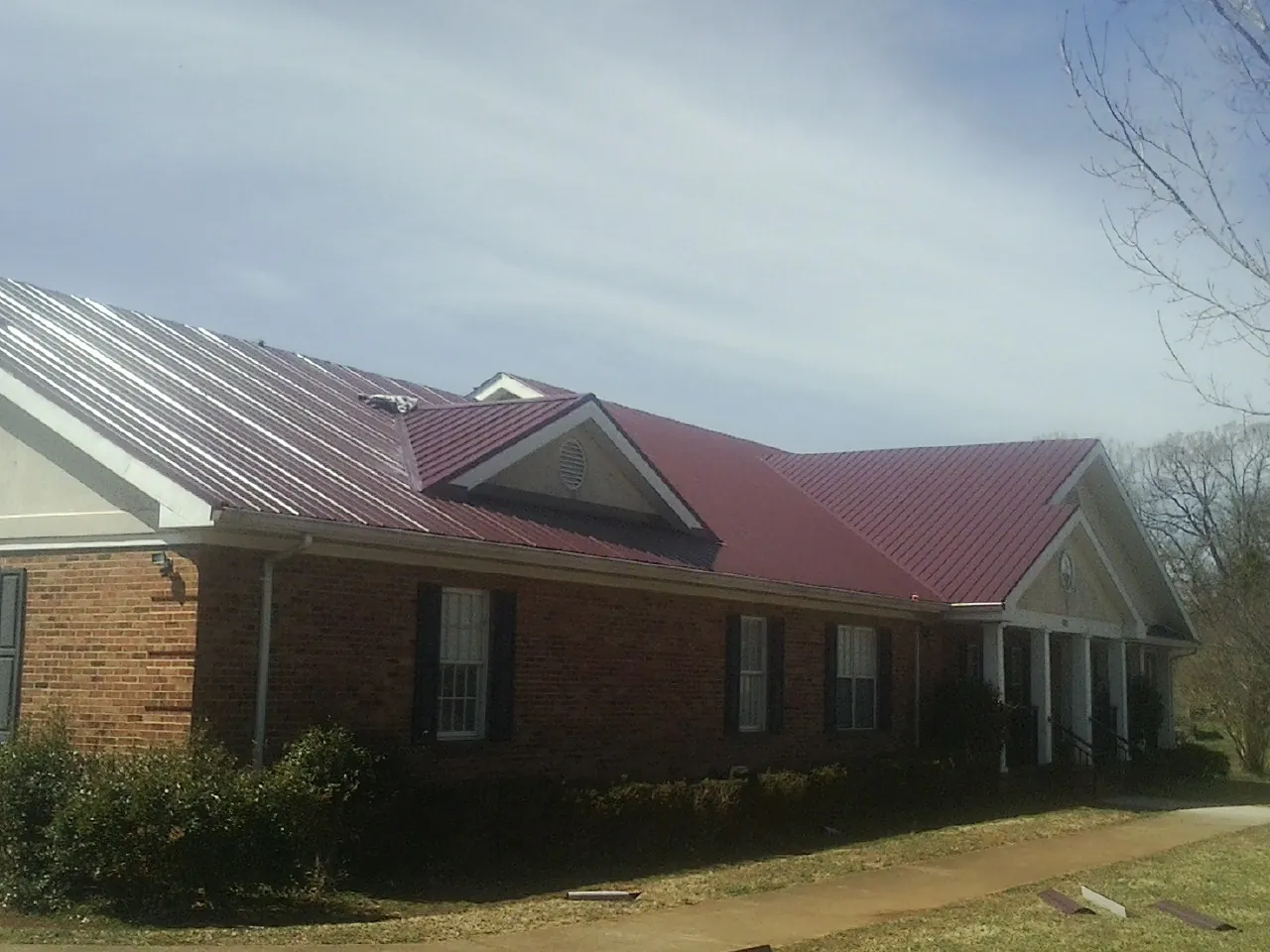 Red metal roof with gabled entries on a long brick building, from a Hail Damage Roof Repair job in Codorus