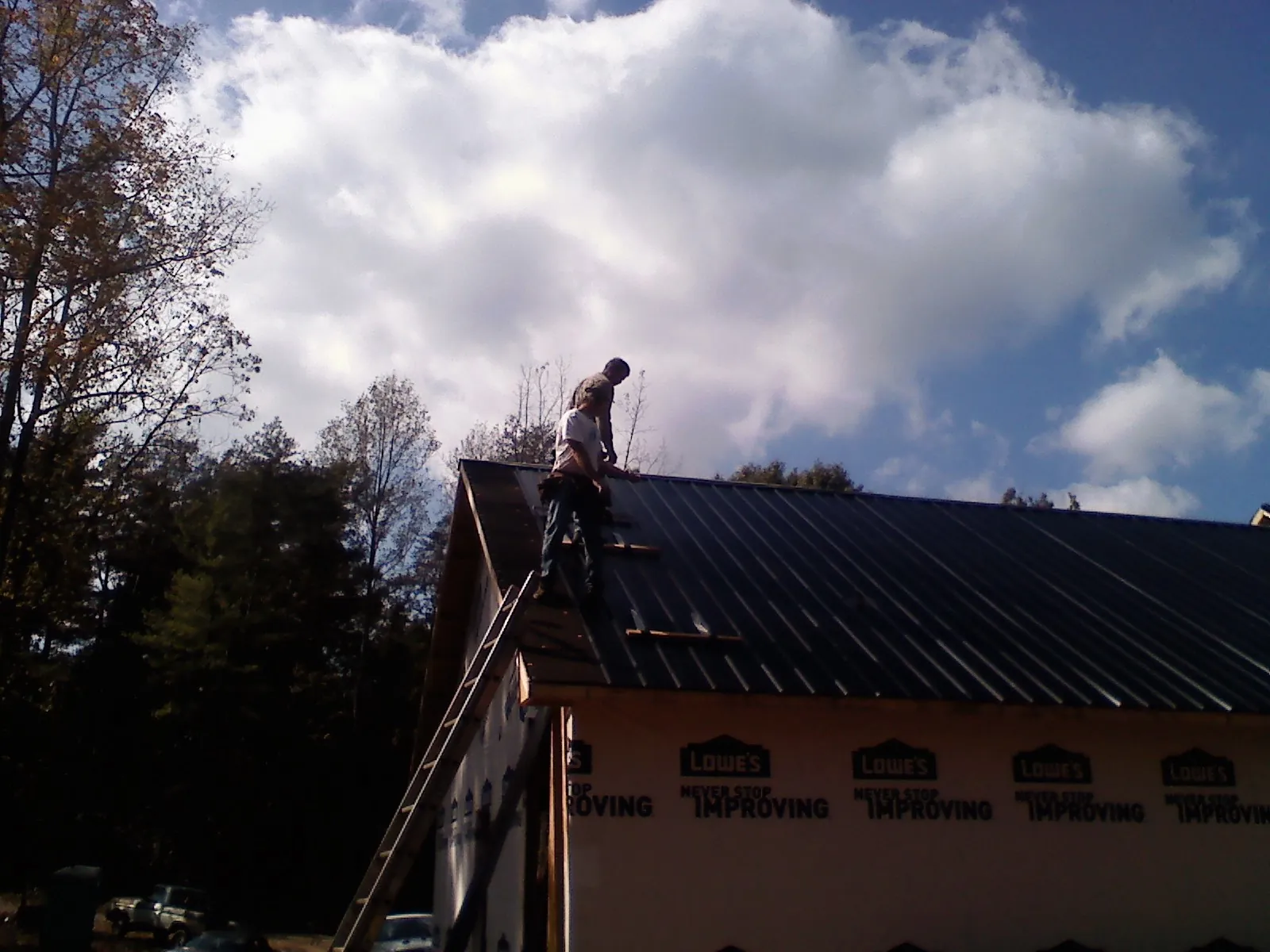 Roofer fastening dark metal panels high against a cloudy sky, from a Roof Inspection job in Codorus
